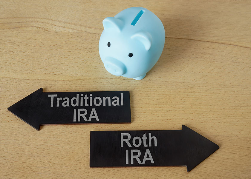 A blue piggy bank on a wooden table with two black arrows labeled Traditional IRA and Roth IRA, pointing in opposite directions. Which IRA is right for you?