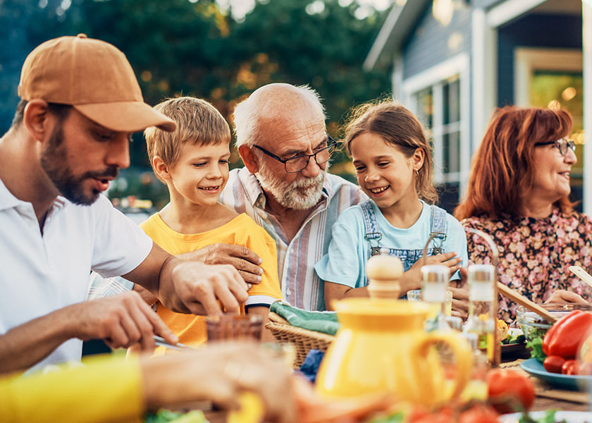 Grandparents with their children and grandchildren enjoying a meal together in their backyard.
