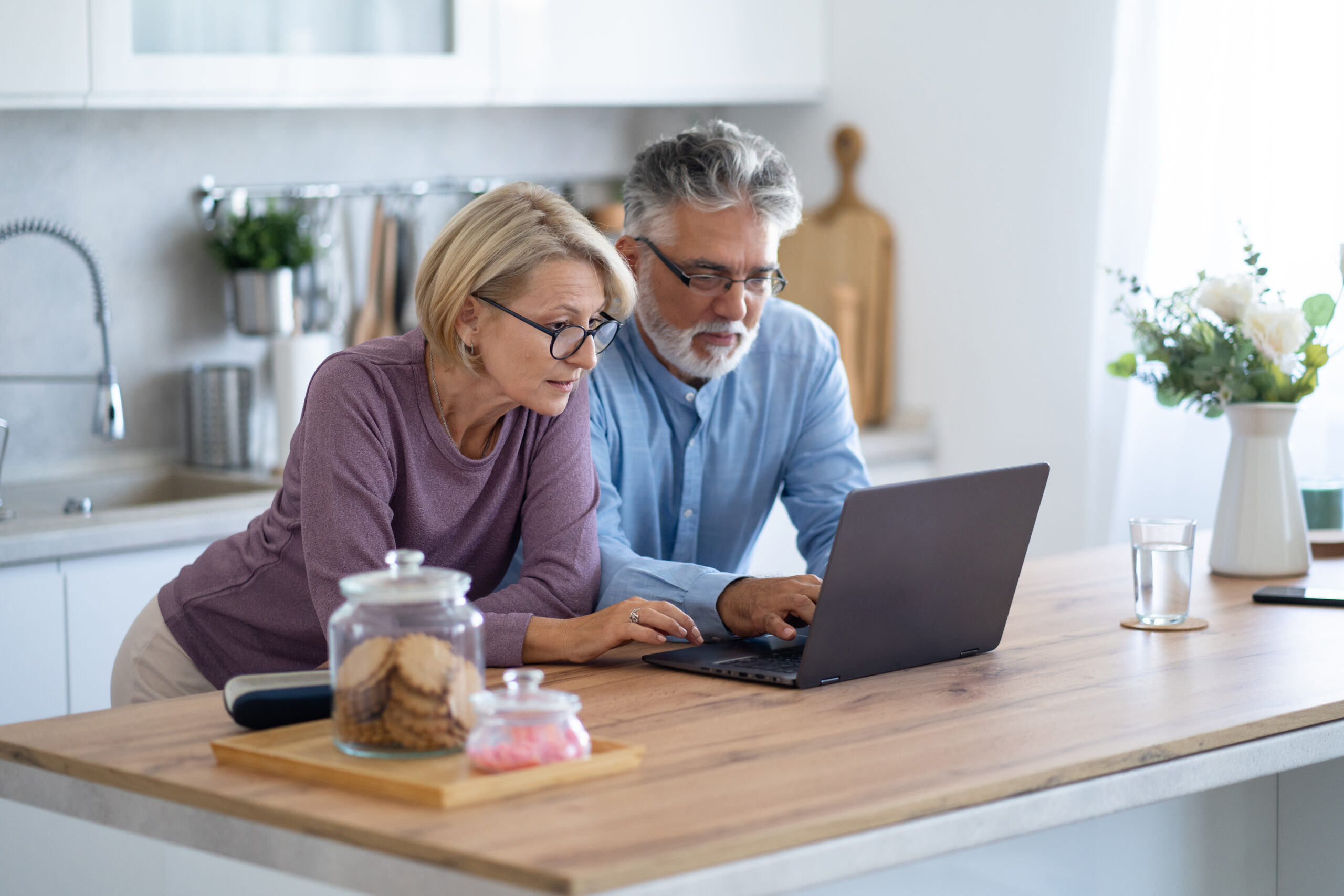 A couple stands at their kitchen island, reviewing information on their laptop, learning more about how the One, Big, Beautiful Bill could impact markets