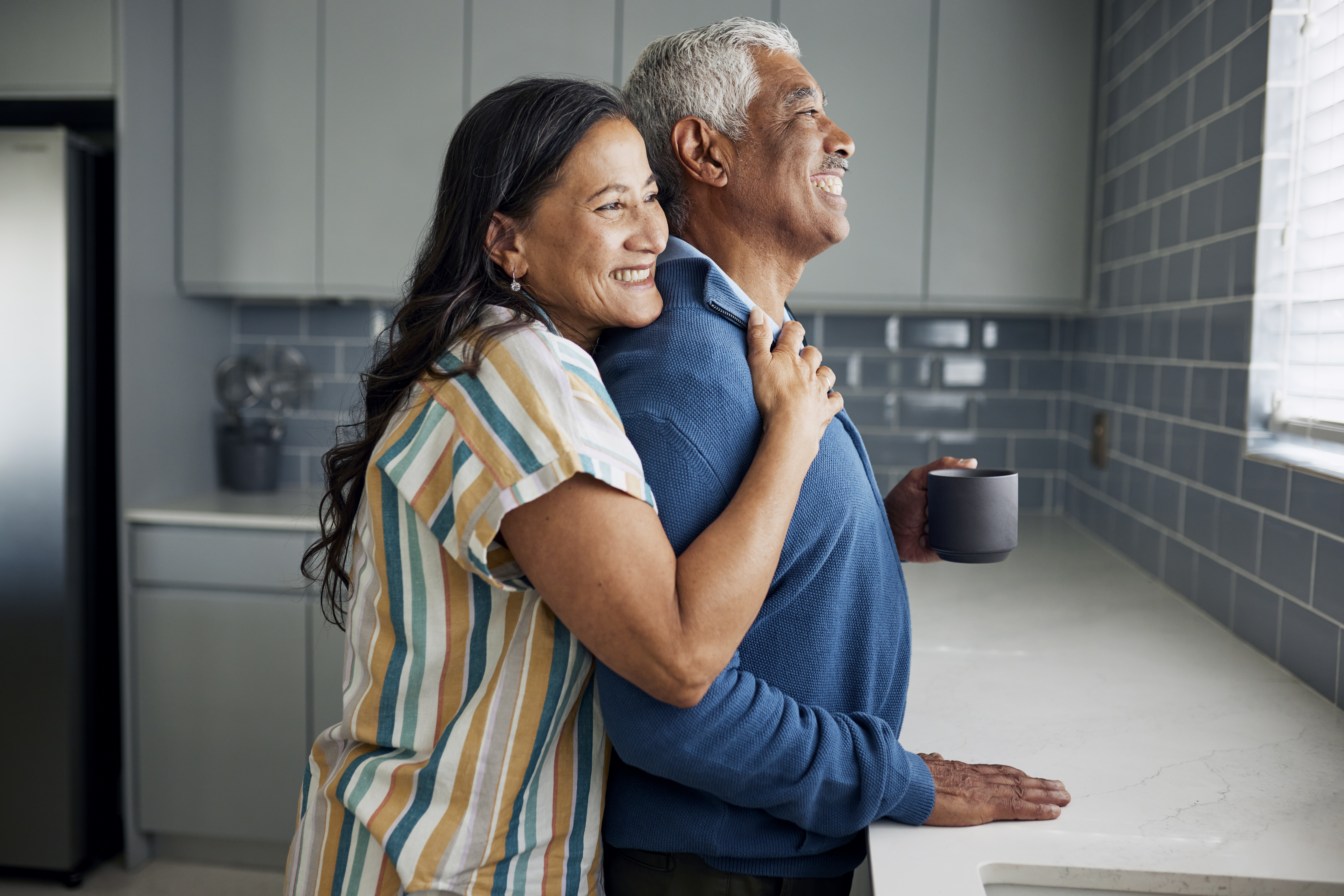 Retired couple in kitchen standing together and looking out the window. Considering Medicare options.